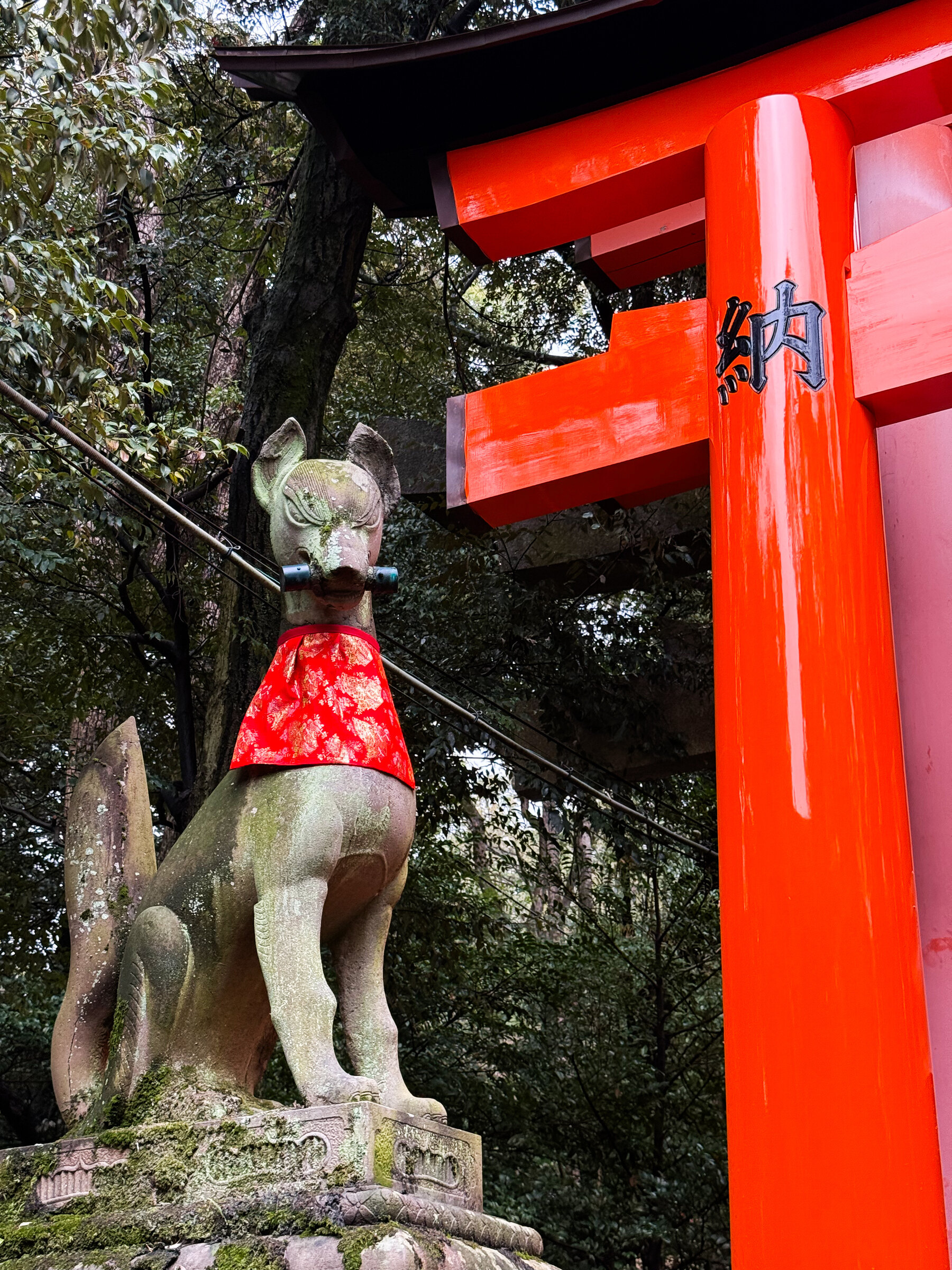 A fox statue beside a vivid red shrine gate.