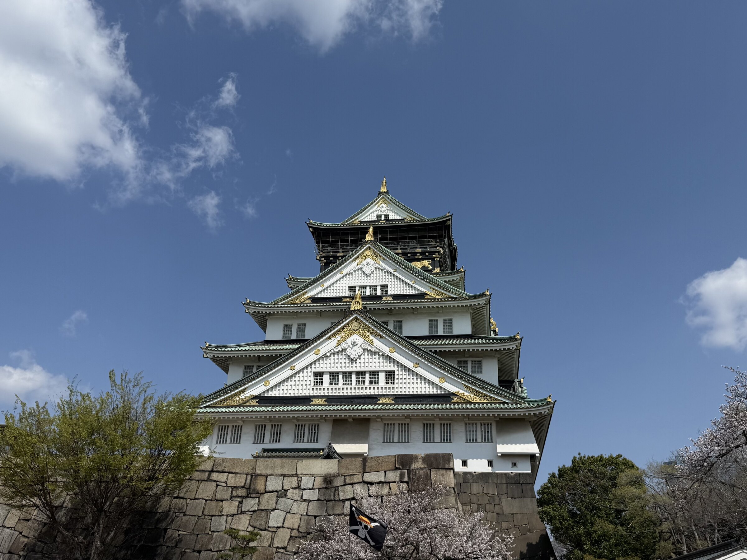 Osaka Castle framed by spring trees and a blue sky.